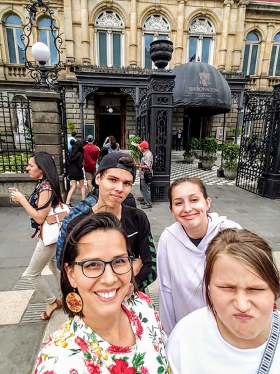 Mother smiles in selfie with her three kids in front of hotel in Florida