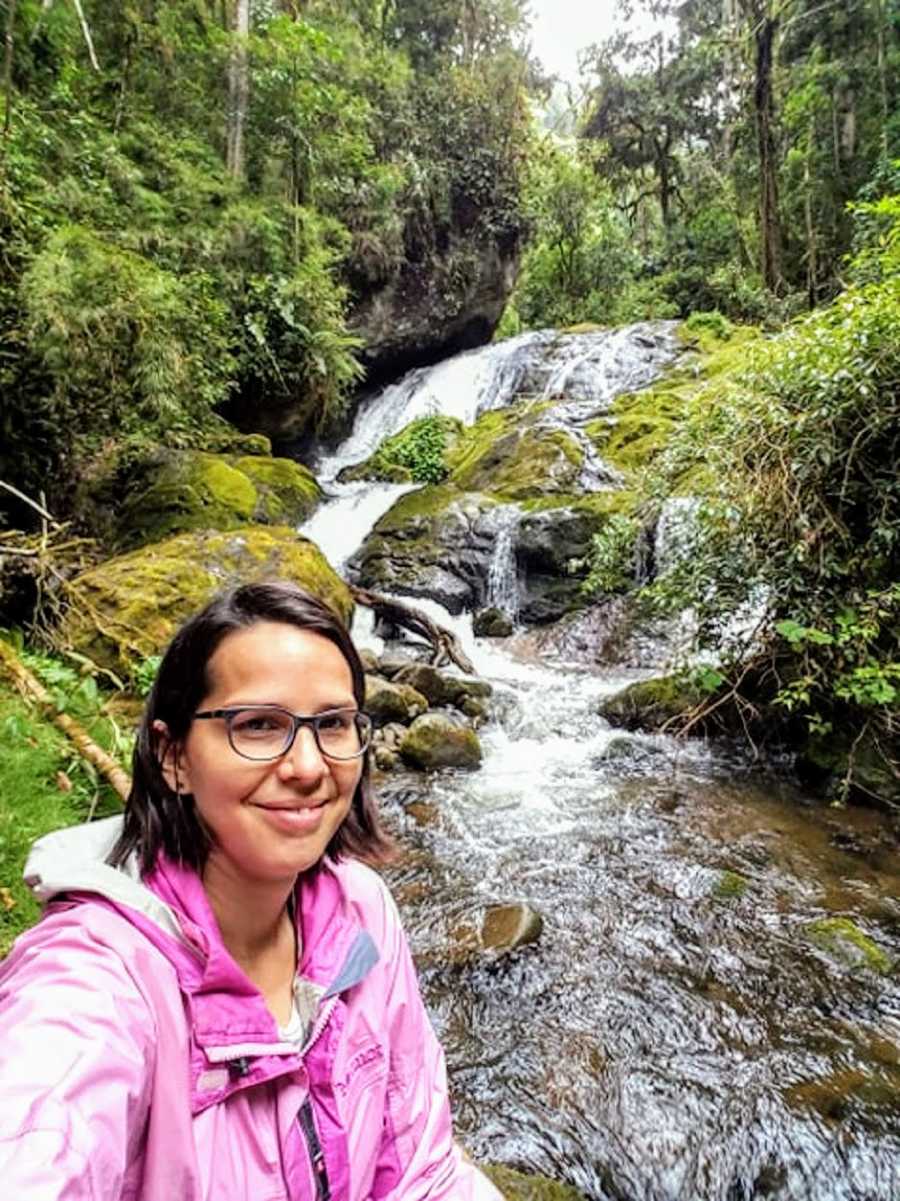 Woman smiles in selfie beside water fall in Costa Rica