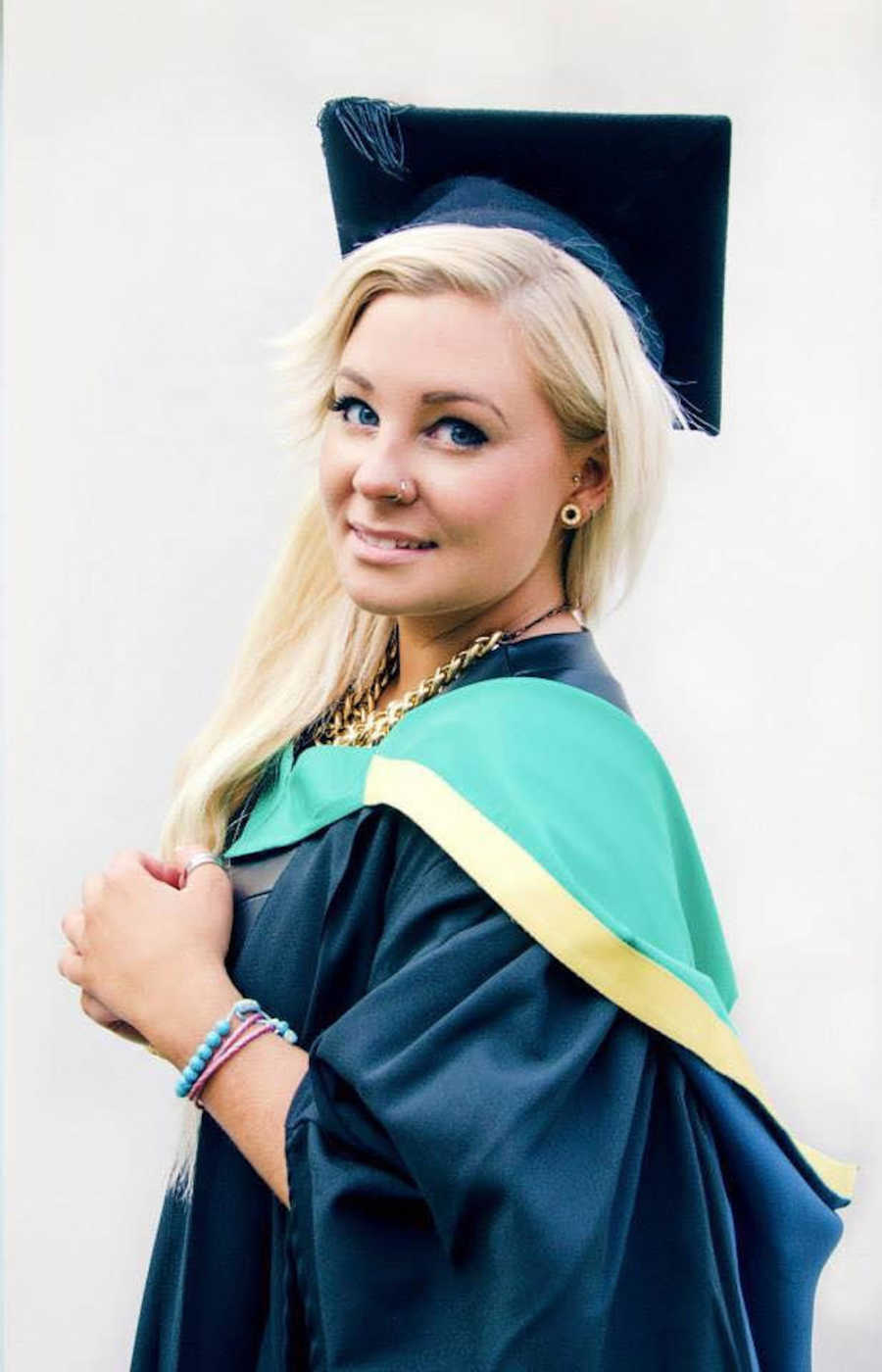 Young woman with BPD and CPTSD stands smiling in cap and gown