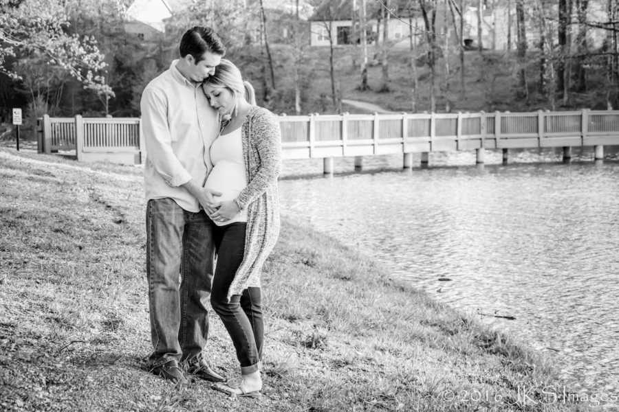 Pregnant woman with eating disorder stands holding stomach with husband beside body of water