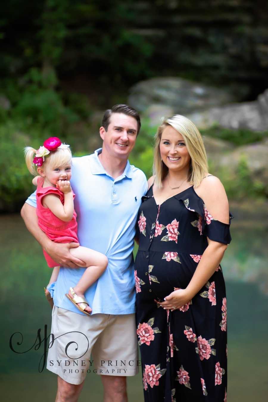 Pregnant woman with eating disorder stands smiling beside husband who holds their young daughter