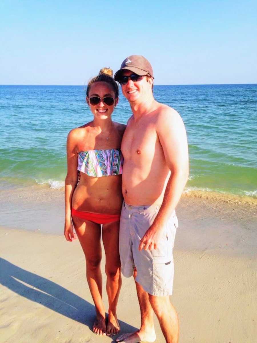 Husband and wife with eating disorder stands arm in arm in bathing suits at beach 