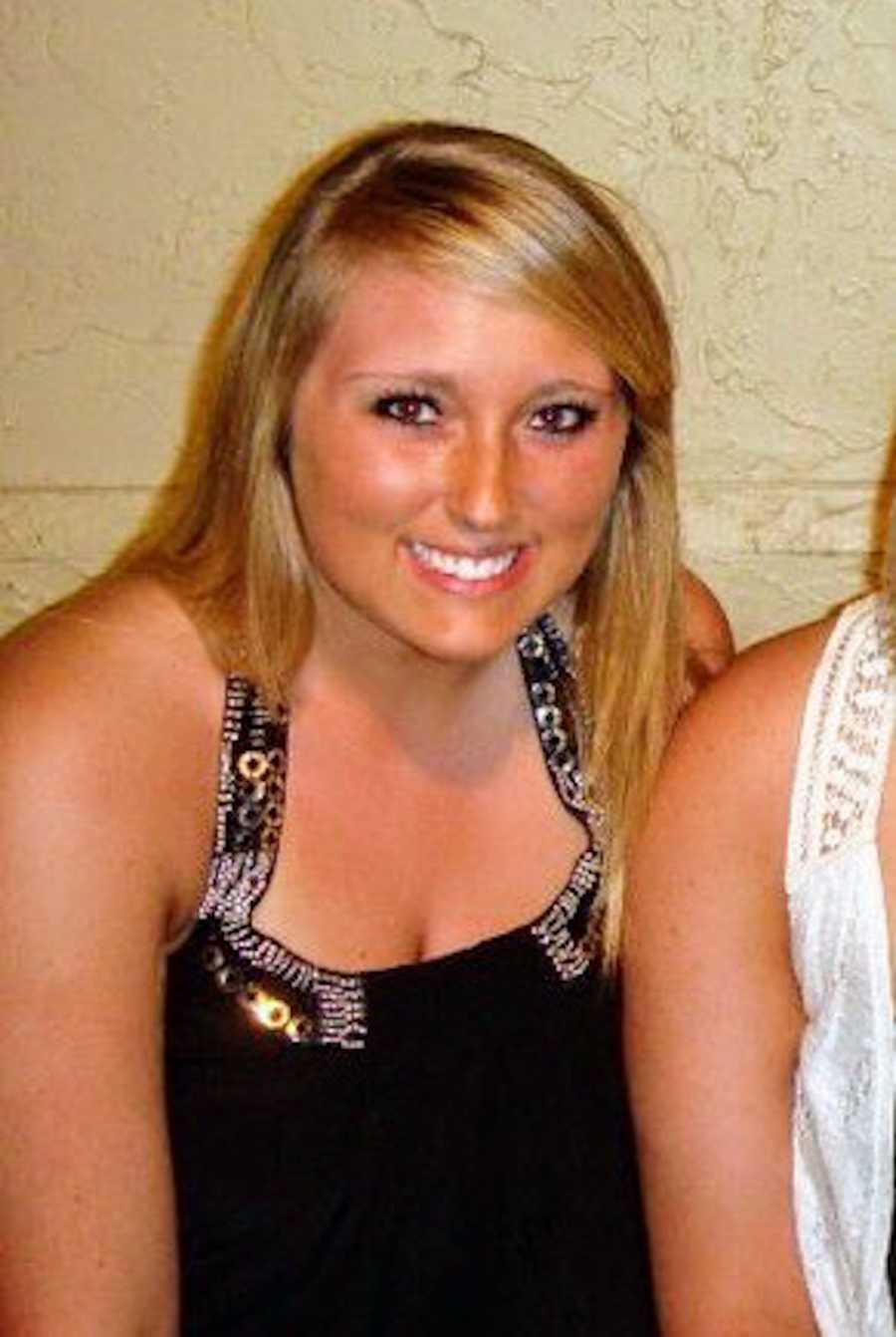 Young woman who struggles with body image sits smiling in black tank top