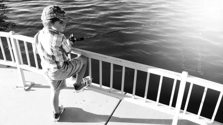 Little boy stands fishing with foot resting on railing