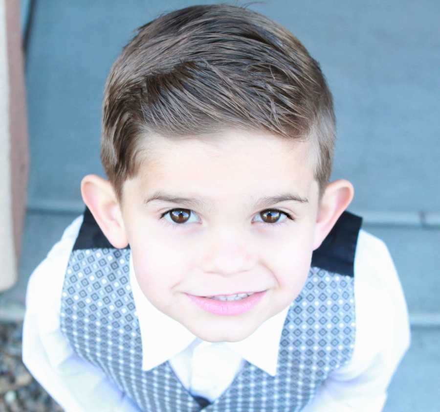 Little boy in formal wear stands smiling as he looks up