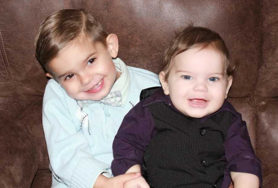 Little boy sits on couch smiling beside his baby brother