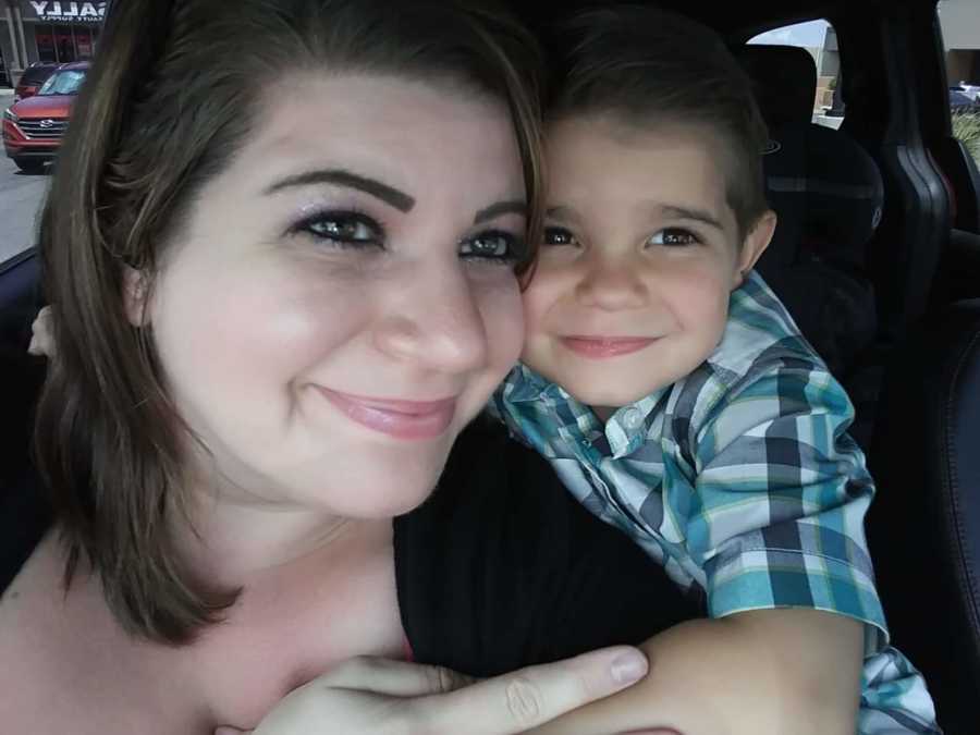 Mother smiles in selfie in car as her young son holds onto her 