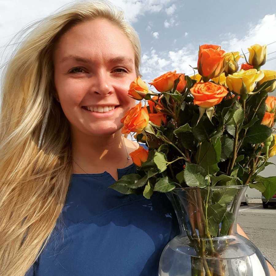 Woman whose husband divorced her stands smiling outside as she holds vase of orange and yellow flowers