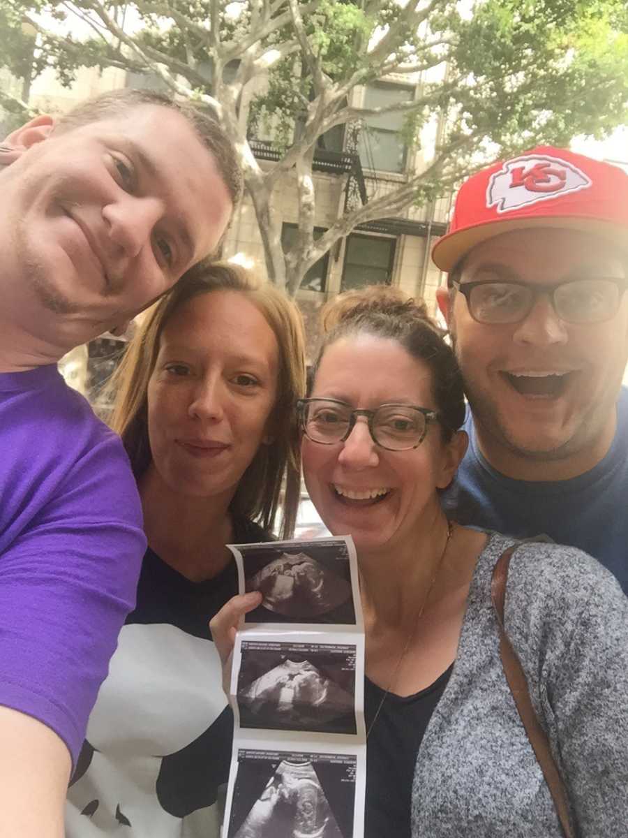Husband and wife smile who are adopting stand smiling holding ultrasound picture besides biological parents