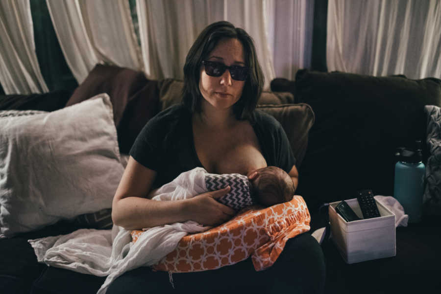 Mother sits on couch in home breast feeding her newborn 