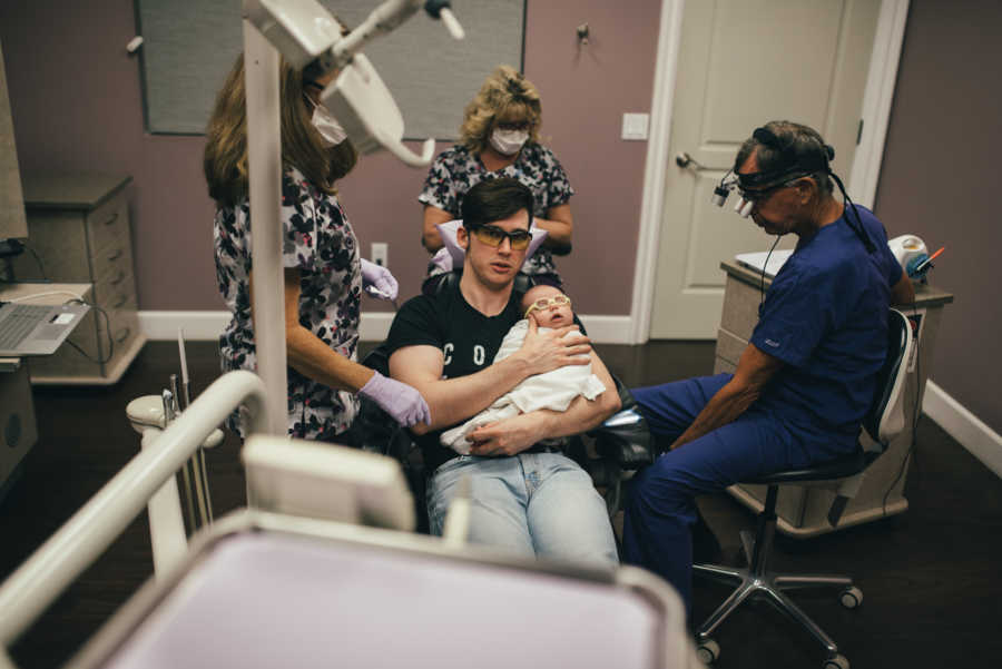 Father sits in IBCLC with three doctors as he holds his baby