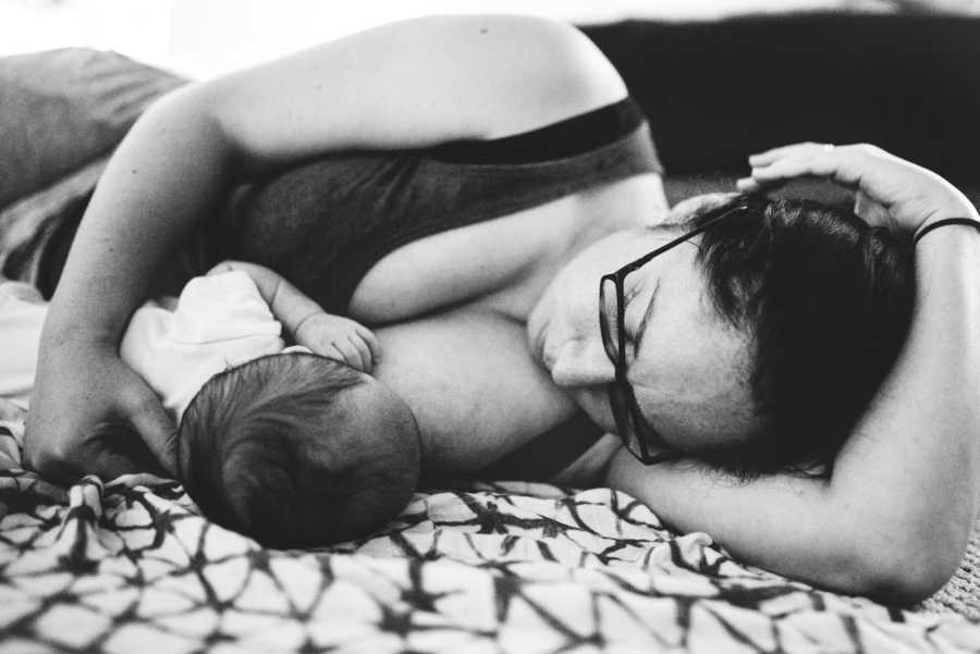 Mother lays on her side on bed while her child breast feeds