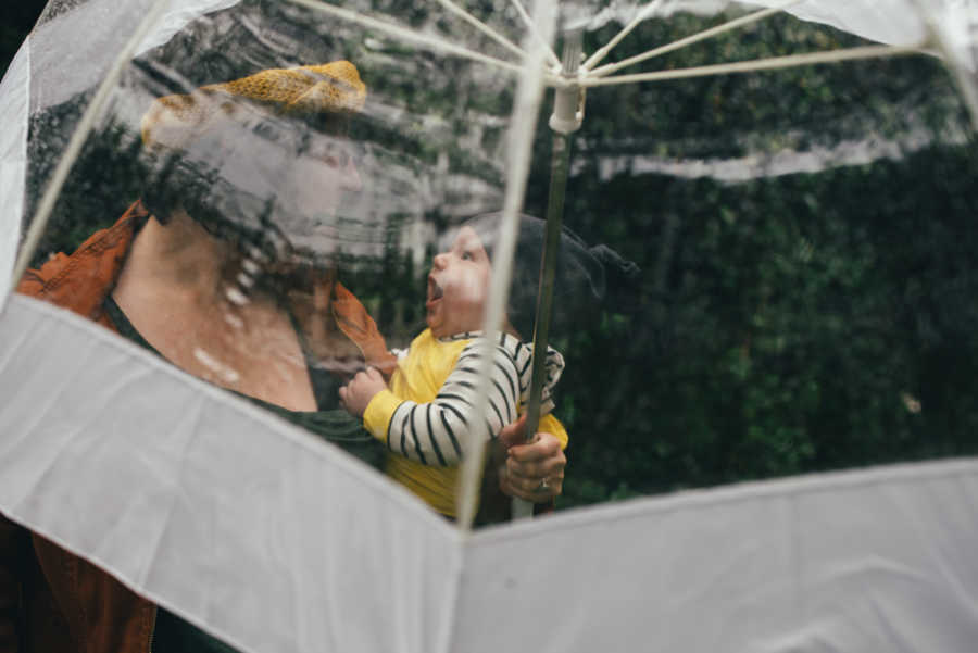 Mother stands under clear umbrella holding her son