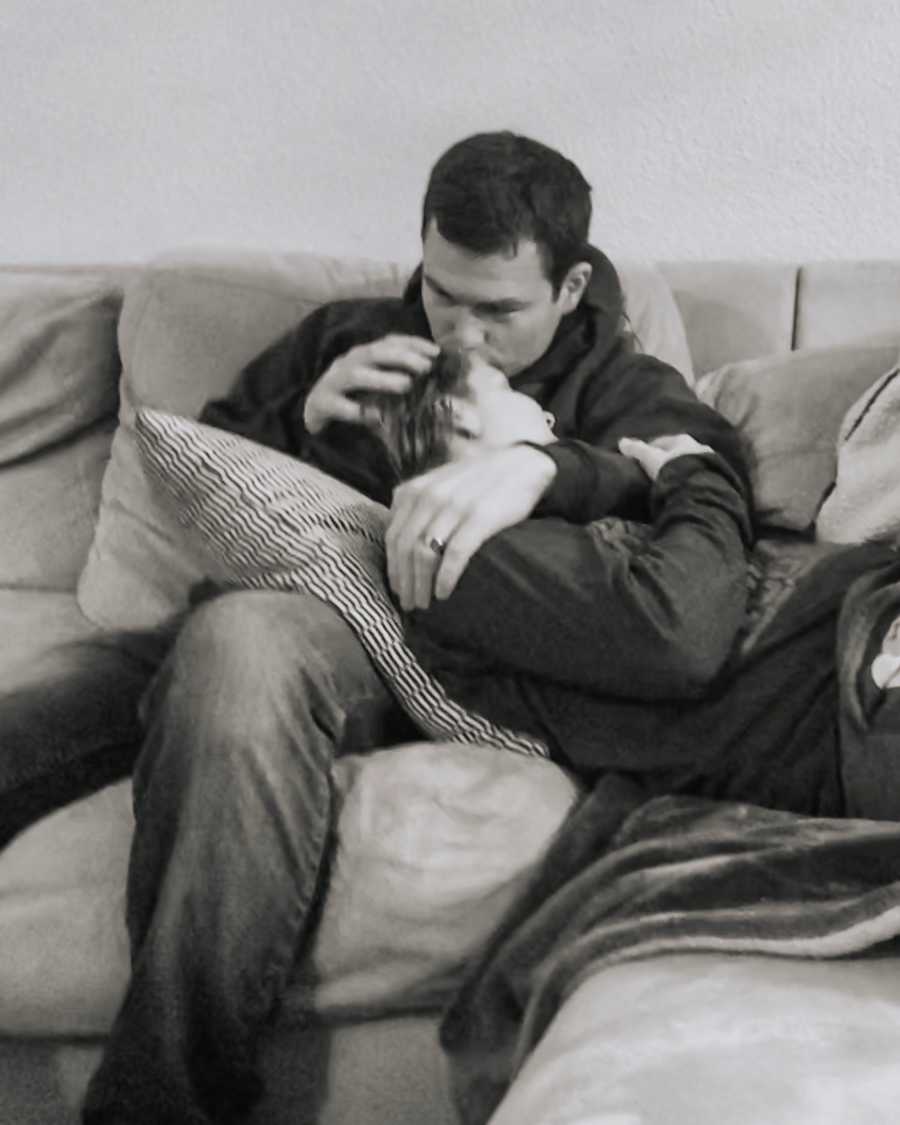 Woman lays on couch with head on lap of husband as he kisses her head