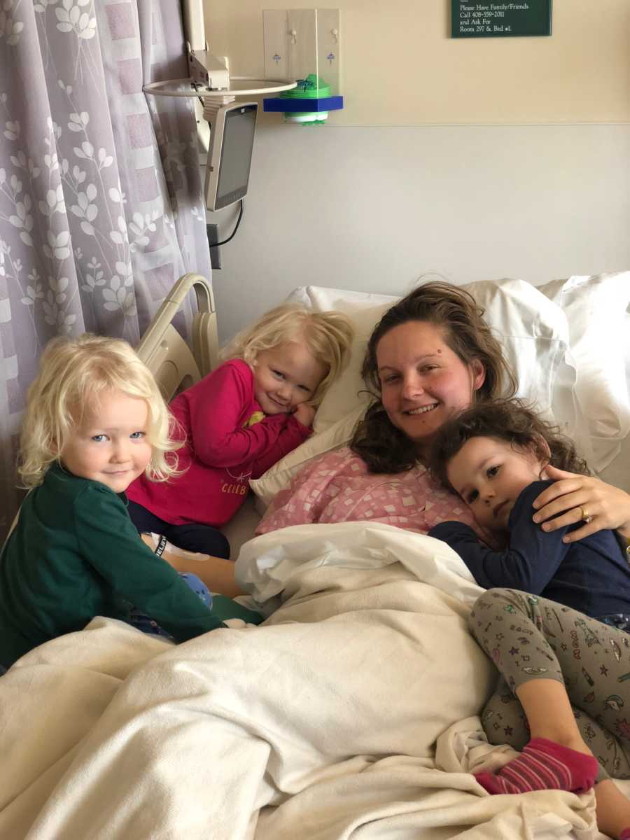 Mother lays in hospital bed with three daughters