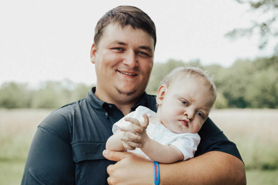 Father stands outside holding son with Kabuki Syndrome,