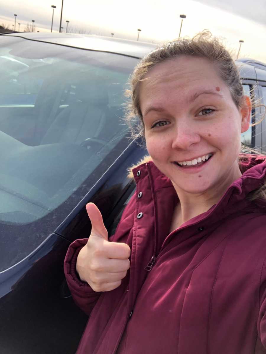 Woman smiles with thumbs up as she takes selfie beside new van that is push start