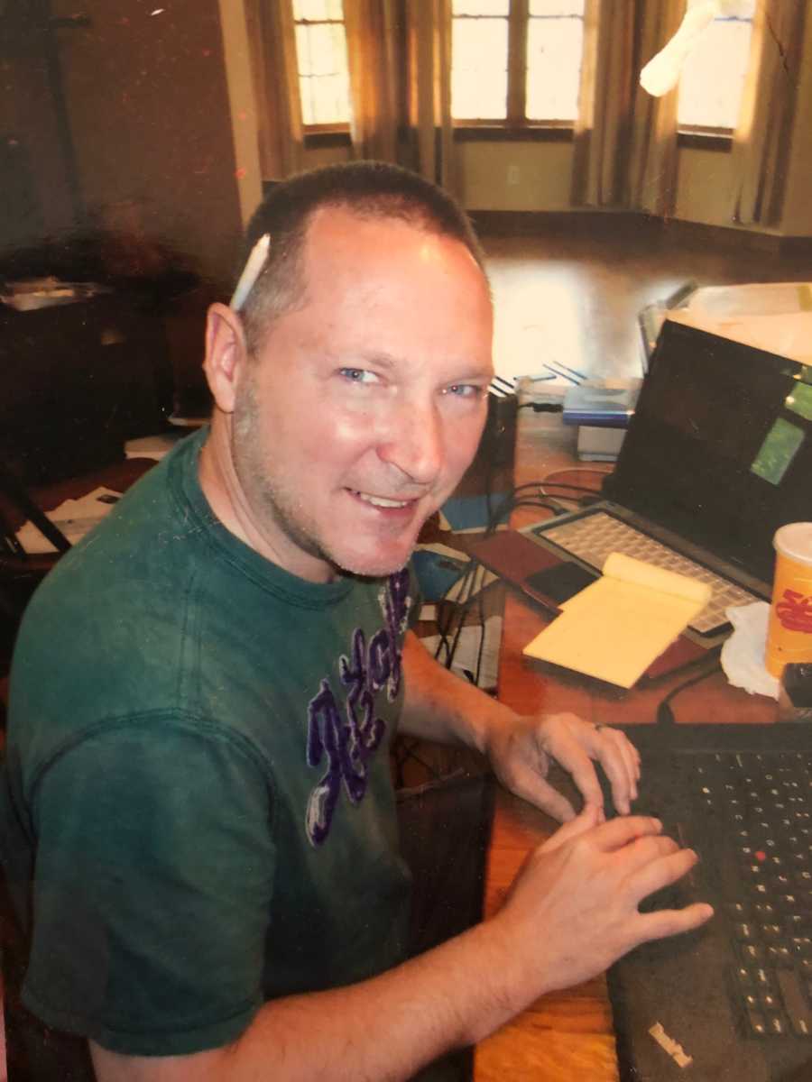 Man who has since passed sits smiling at desk with computers