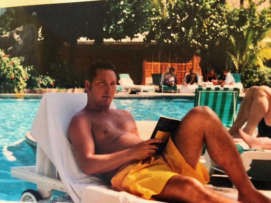 Man who has since passed sits on lounge chair by pool reading a book