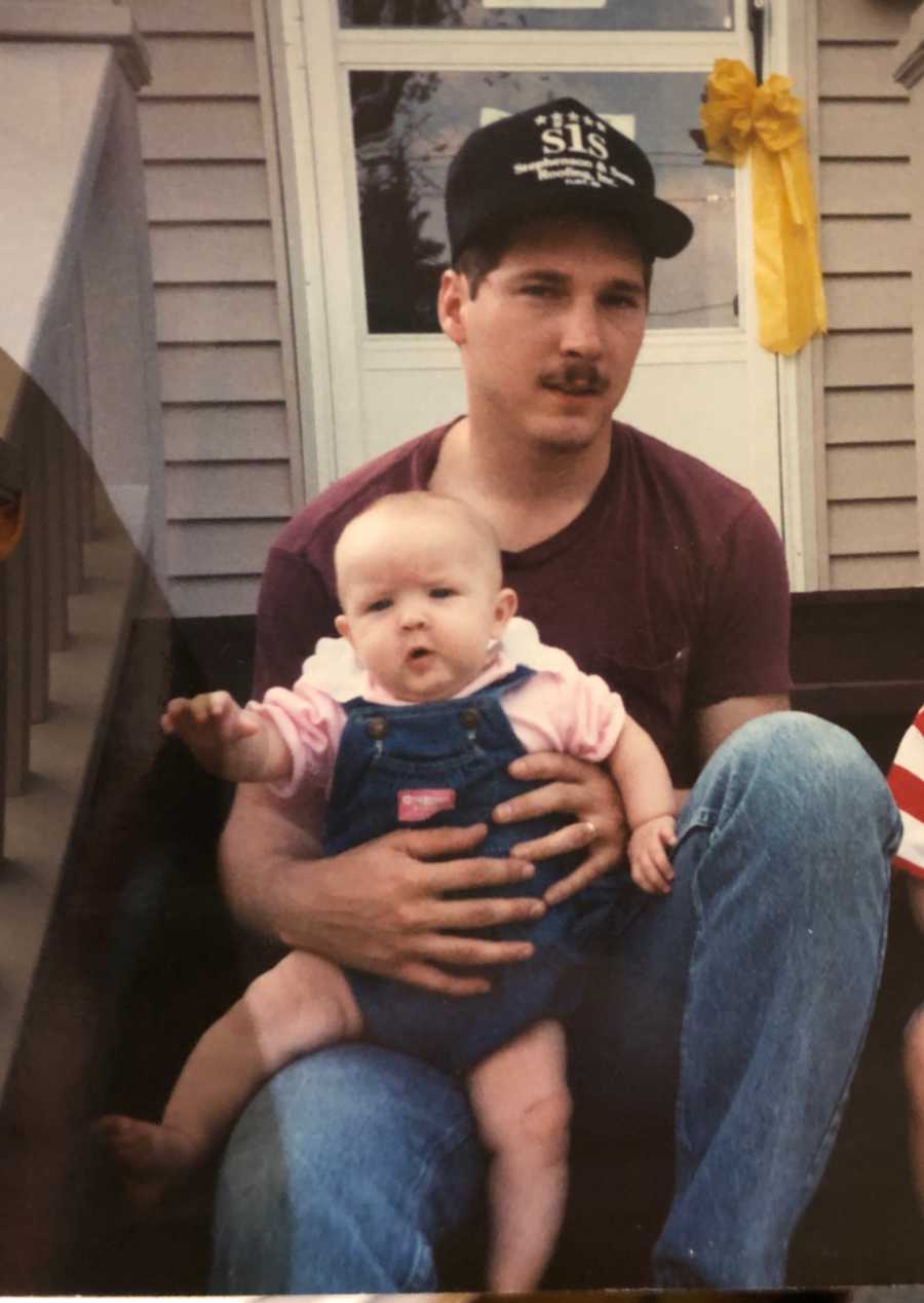 Man who has since passed sits outside on steps of home with baby daughter on his lap