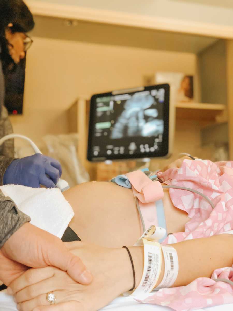 Woman lays in hospital bed with birthing band on as she holds husband's hand during ultrasound