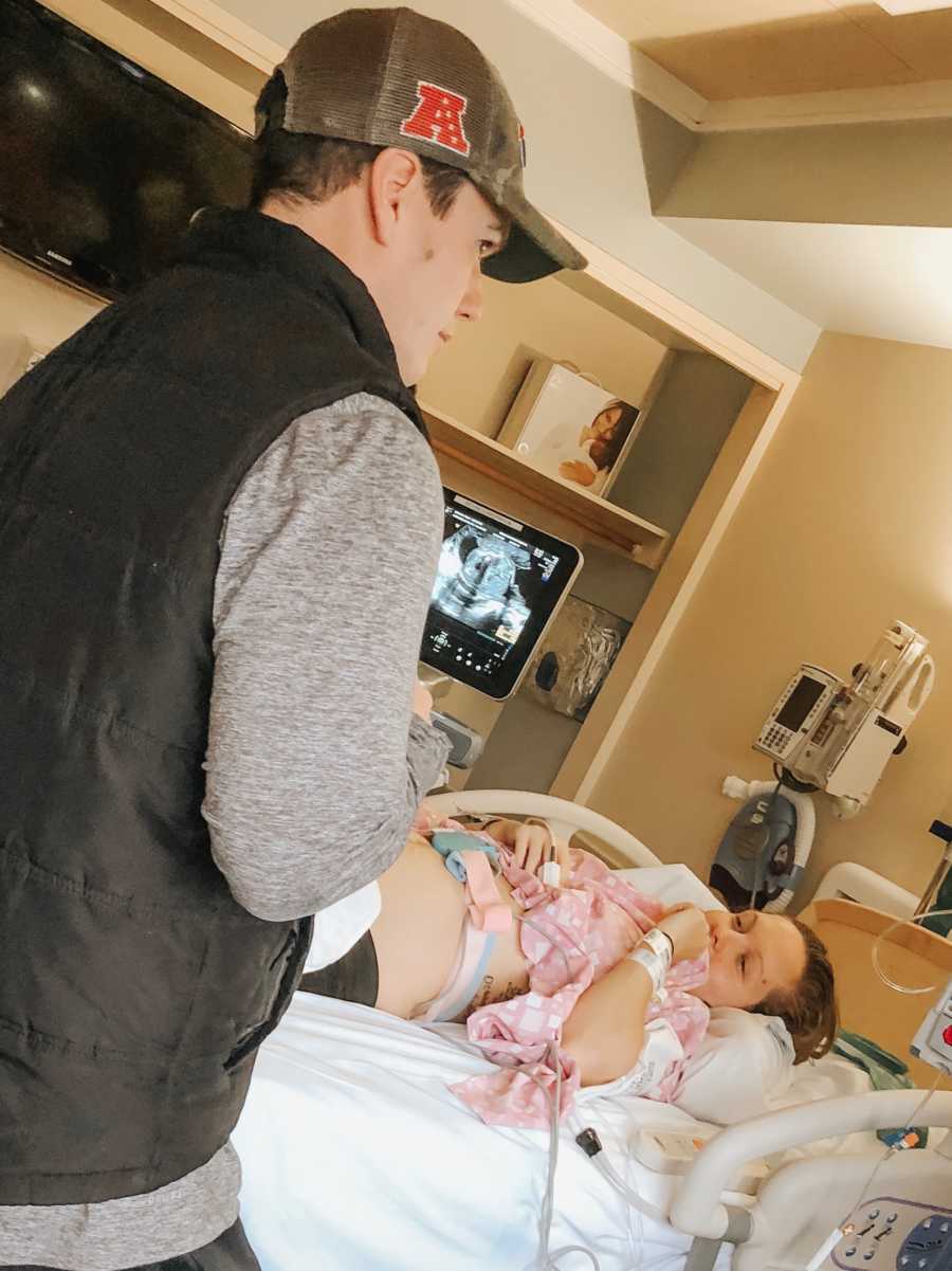 Husband stands beside hospital bed where his wife lays