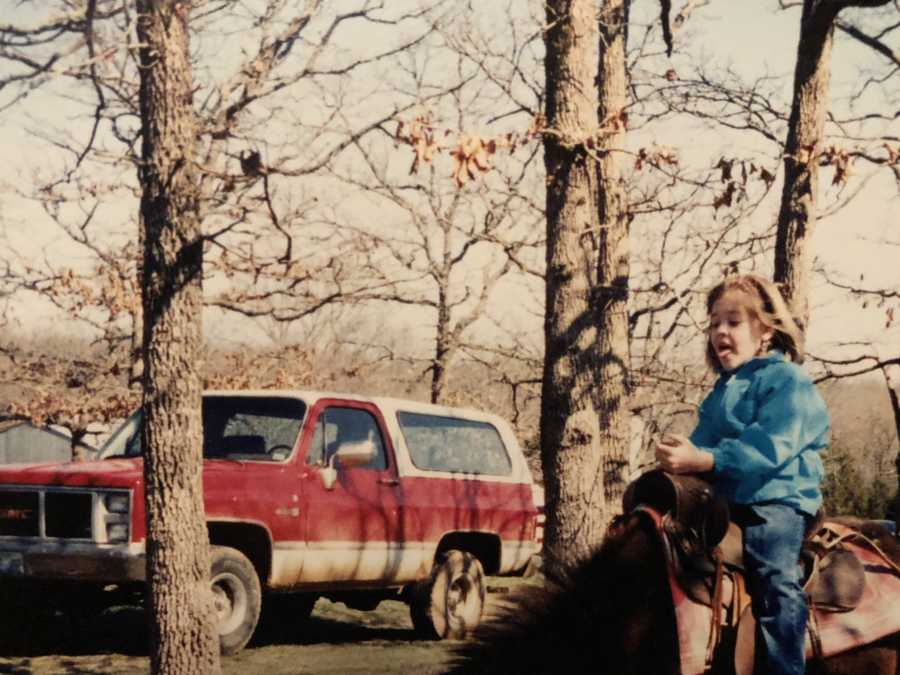 Little girl sits on horse outside with red car in background