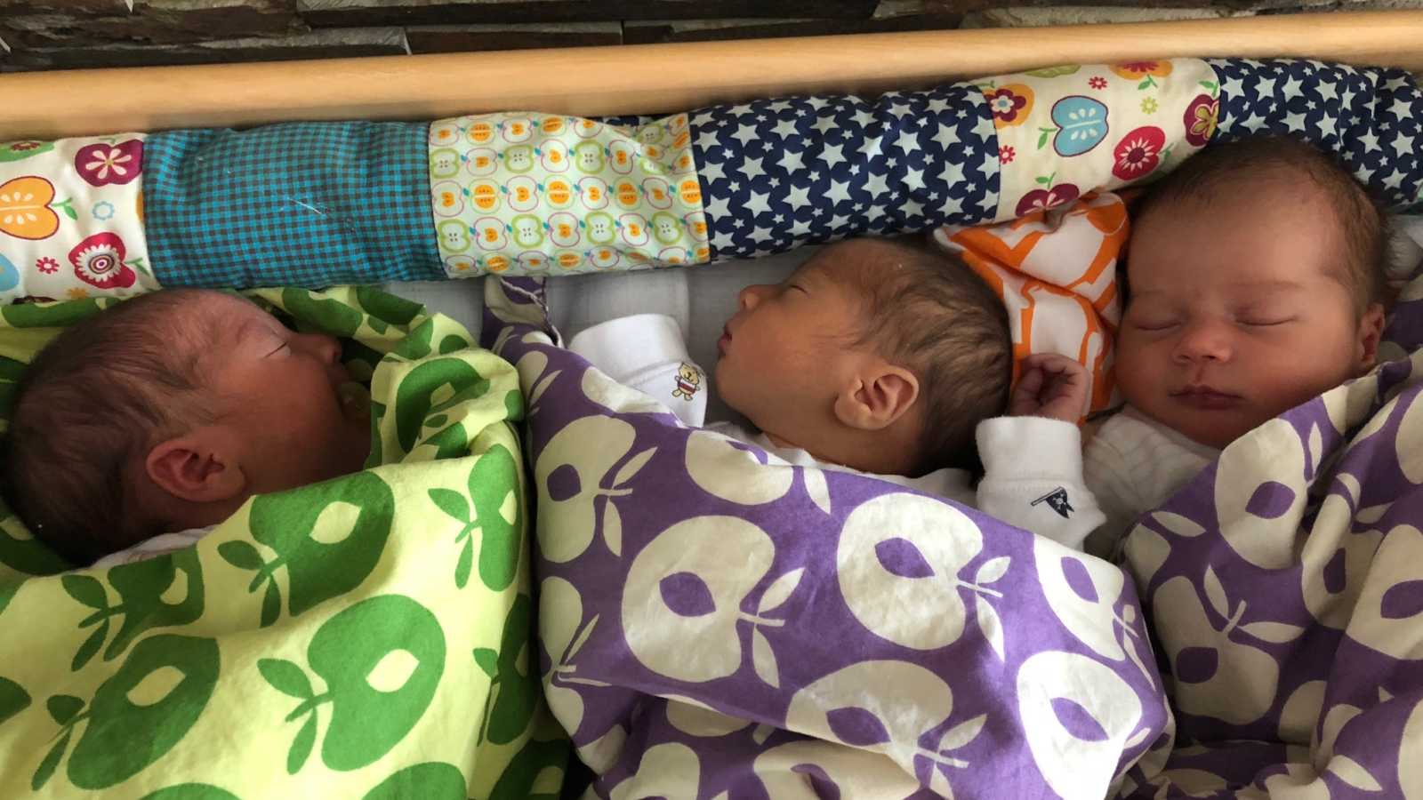 Baby triplets lay asleep in crib all wrapped in their own blankets