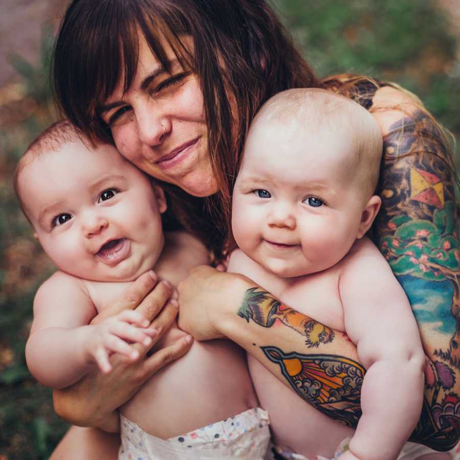 Mother smiles as she holds twin babies in her arms