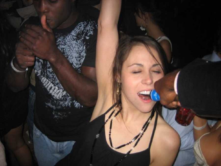 Woman who was a binge drinker stands with arm in air and mouth open as someone pours alcohol into her mouth