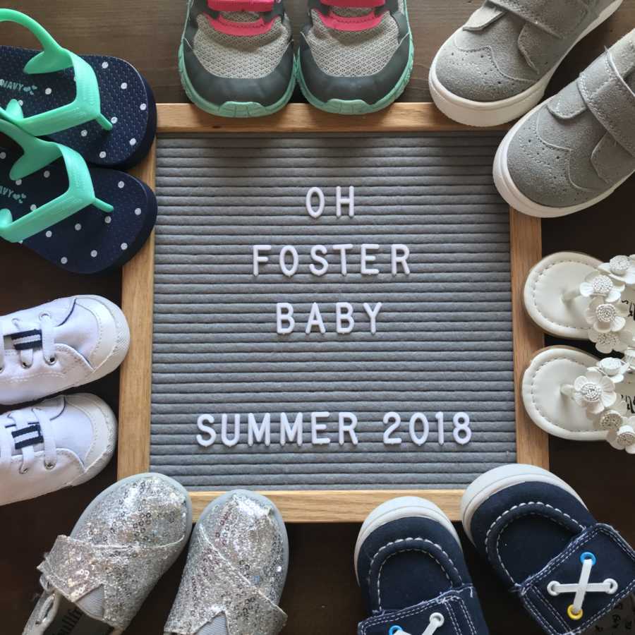 Sign laying on ground that says, "oh foster baby summer 2018" with baby shoes surrounding it