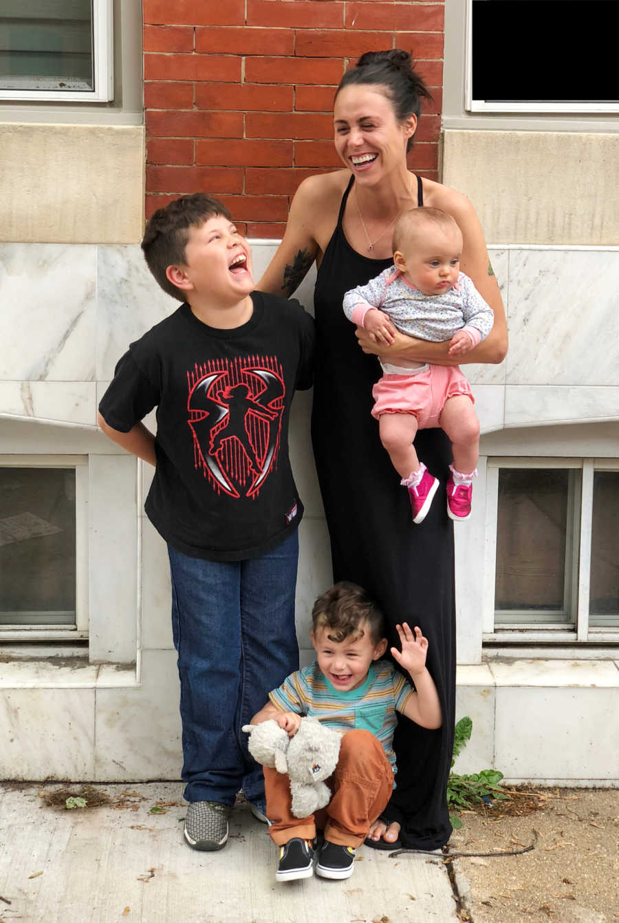 Mother who has joined alcoholics anonymous stands smiling outside with her three children