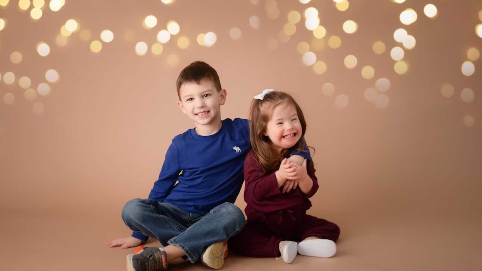 Little boy sits on ground with arm around his little sister with down syndrome for photoshoot