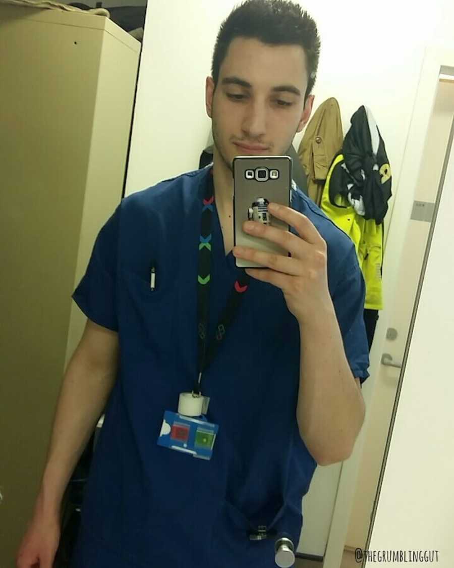 Man with Crohn's disease wearing scrubs stands taking mirror selfie
