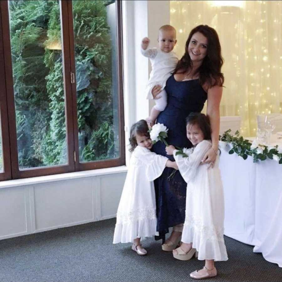Woman stands at child's christening holding baby while her two oldest stand at her side