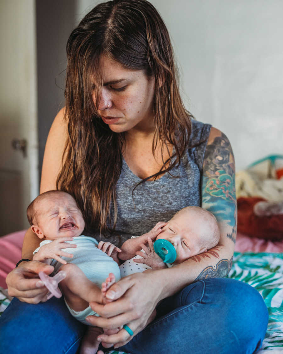 Woman sits in bed of home holding baby twins in her arms