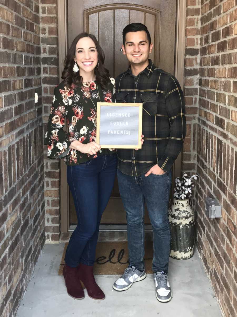 Husband and wife stand outside front door with sign that says, "licensed foster parents"