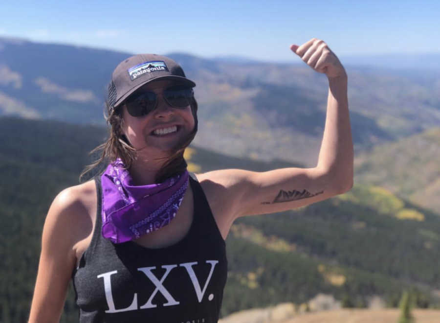 Woman with Cystic Fibrosis stands smiling as she flexes her arm with mountain tattoo