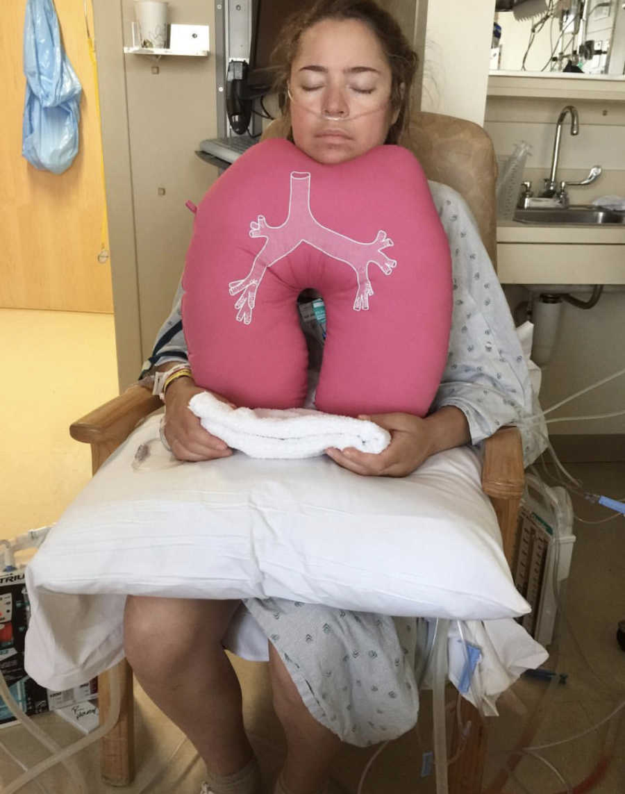 Woman with Cystic Fibrosis sits in chair in hospital room resting chin on pillow that looks like lungs
