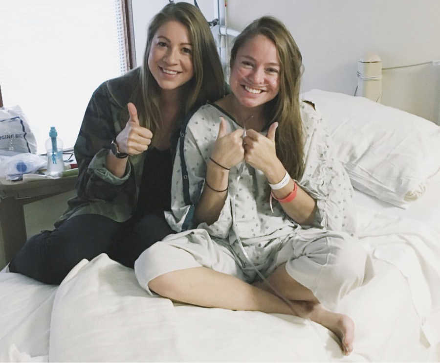 Woman with Cystic Fibrosis sits on hospital bed beside another woman and they both have thumbs up