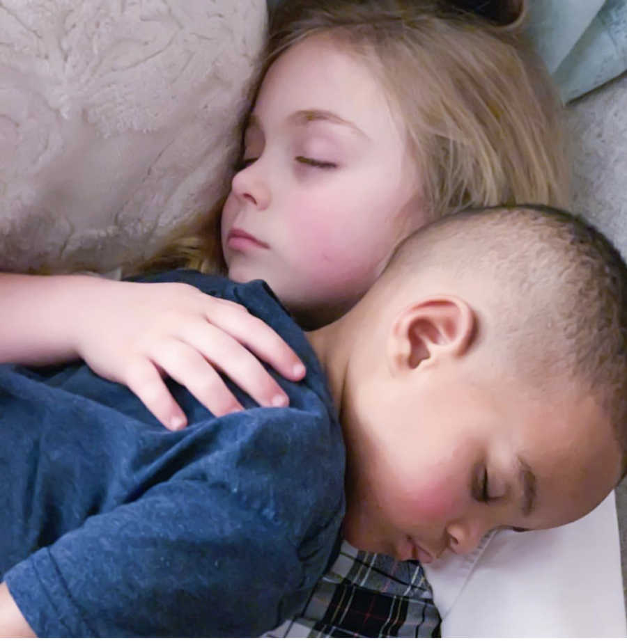 Little girl lays asleep on back with adopted baby brother on top of her