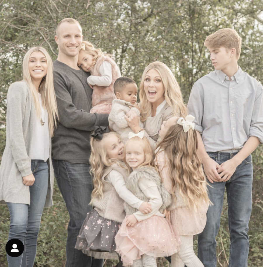 Husband and wife stand outside smiling with their seven children