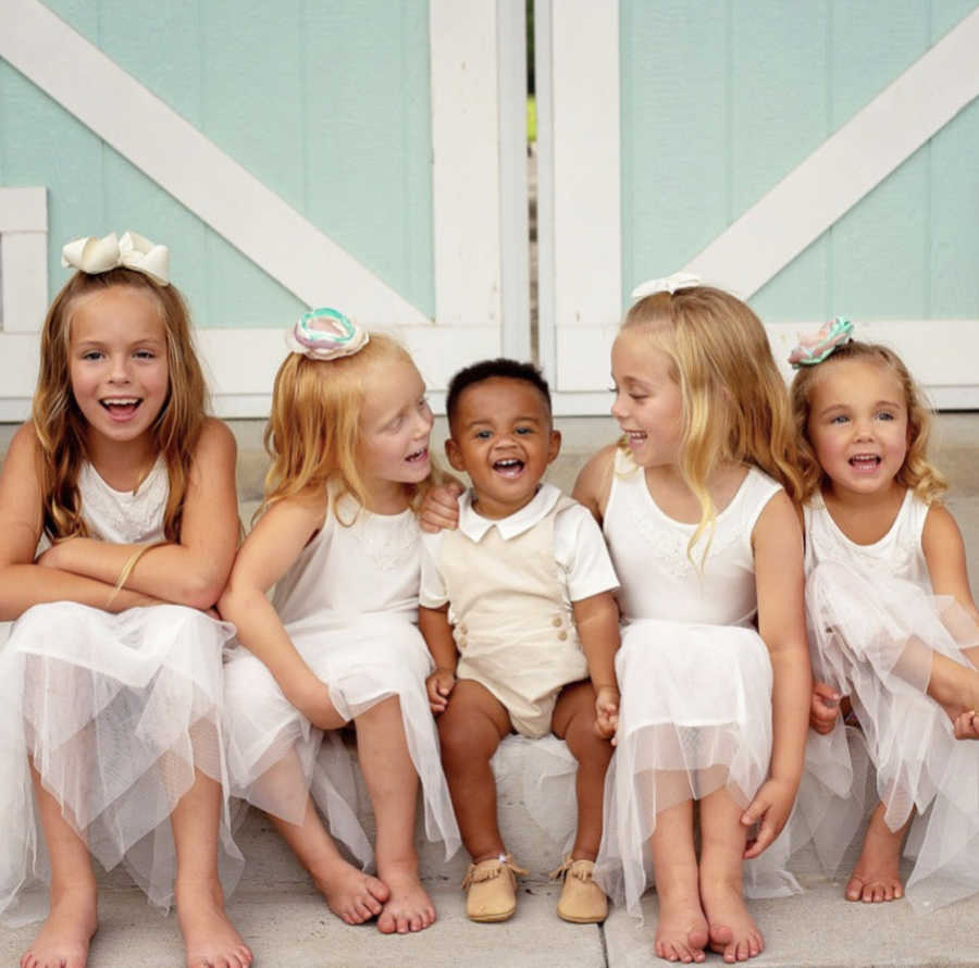 Four sisters sit outside with their adopted baby brother sitting between them