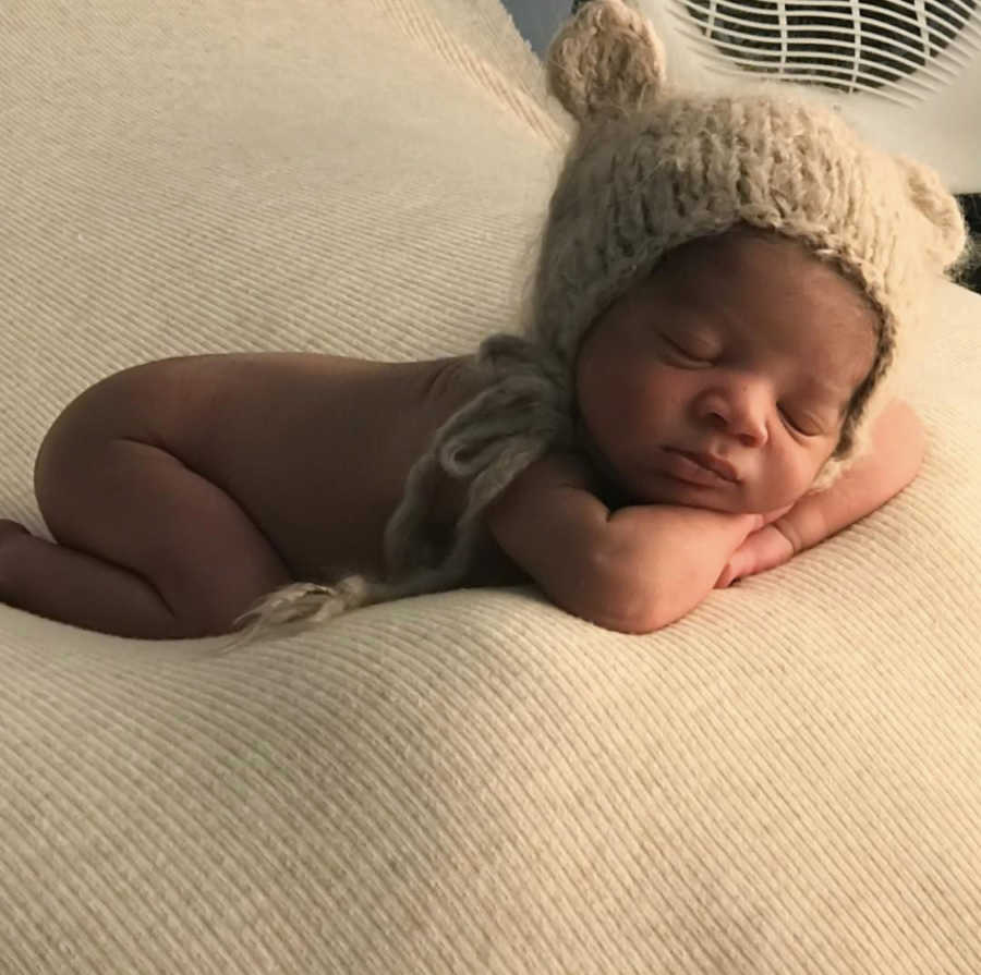 Adopted newborn lays curled up asleep on blanket with nothing but knit hat on