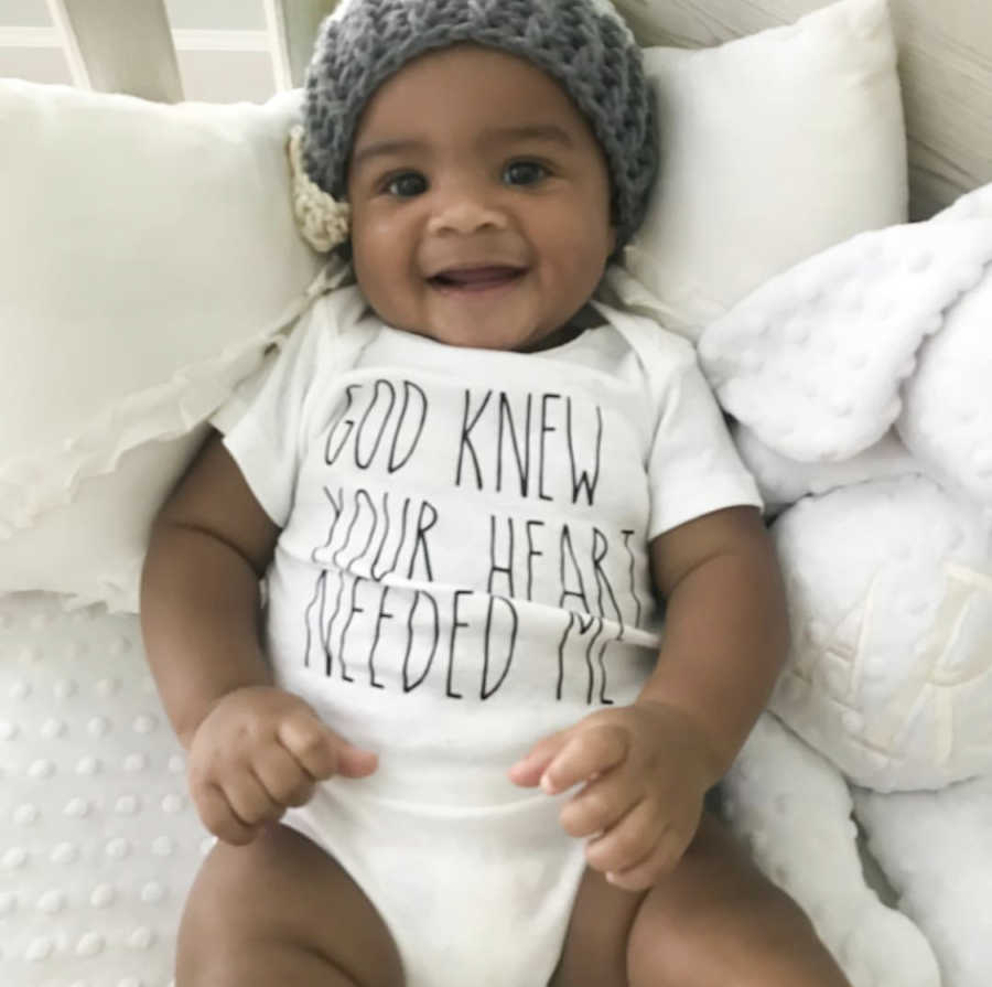 Adopted newborn lays on back smiling as he sits in crib in home