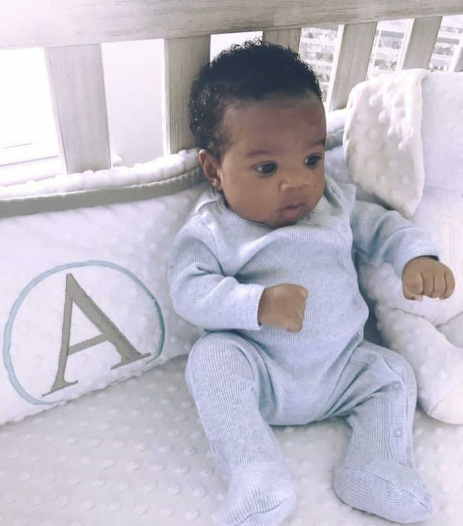 Adopted newborn sits up in crib in home