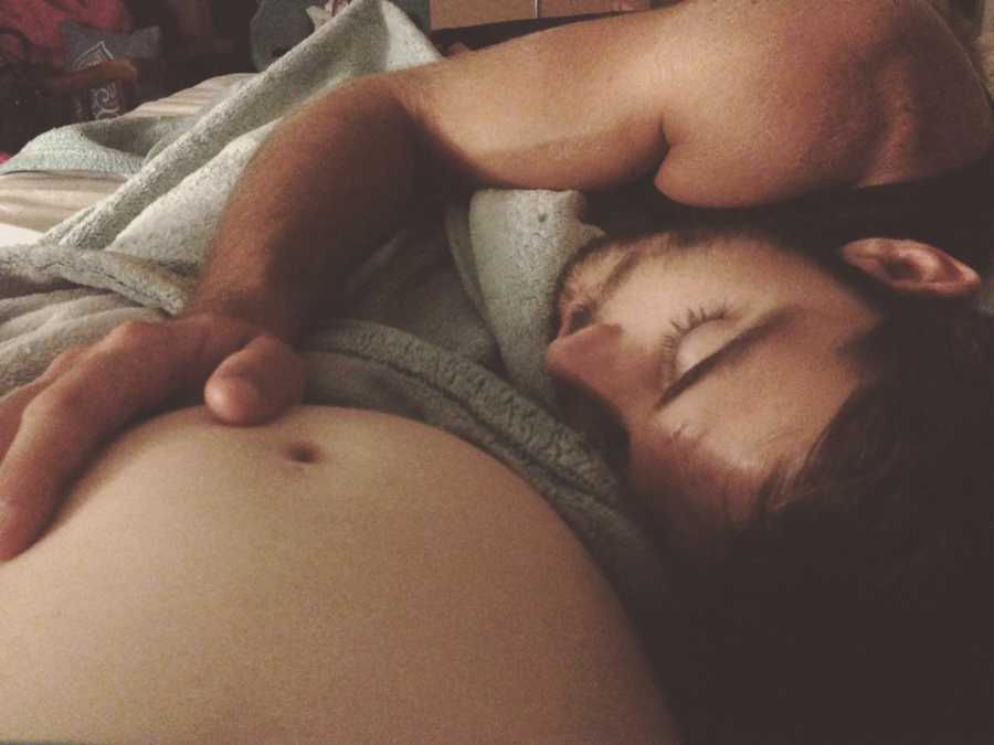 Husband lays asleep beside wife with his hand on her pregnant stomach