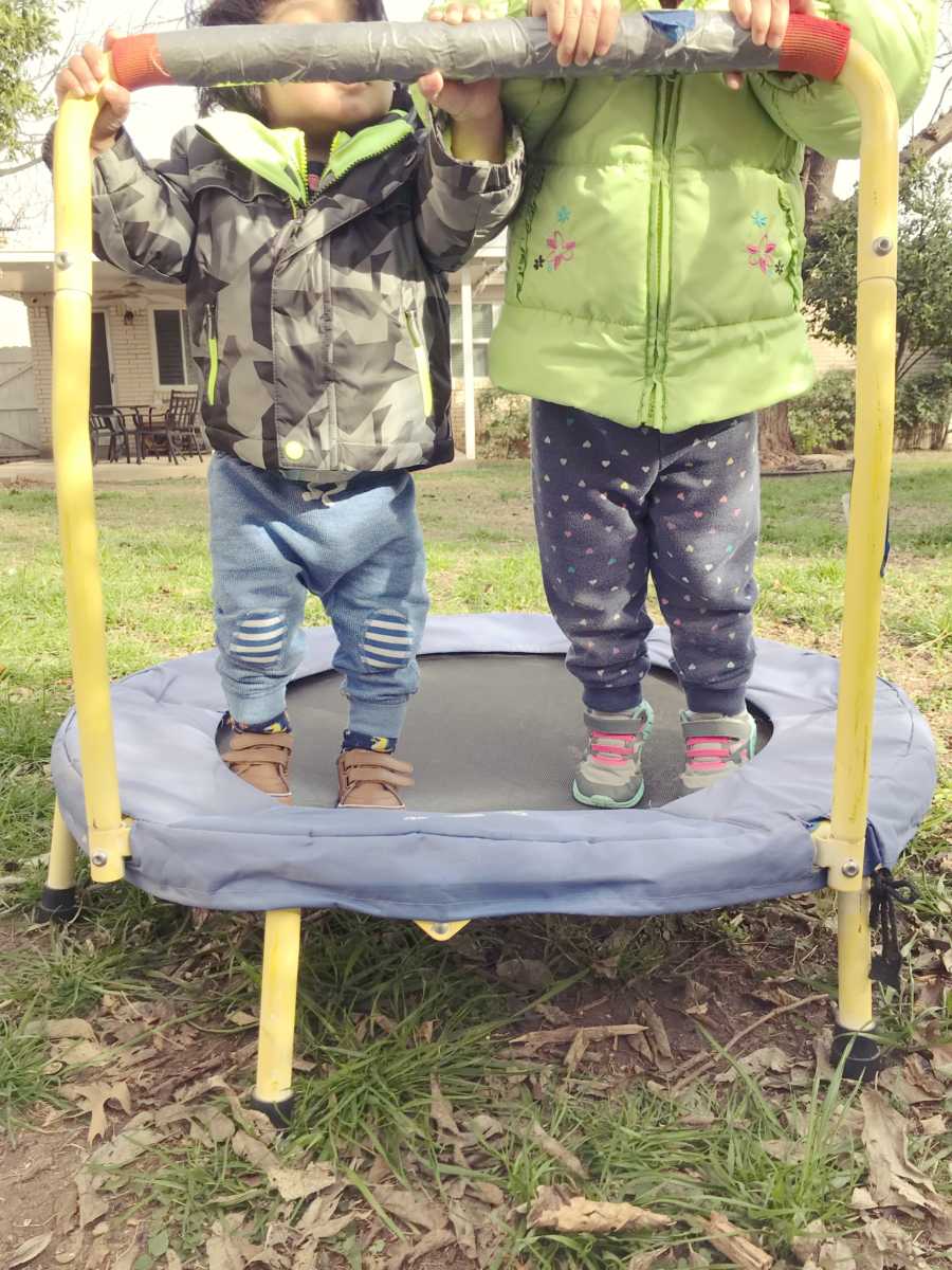 Foster siblings stand on mini trampoline in yard of home