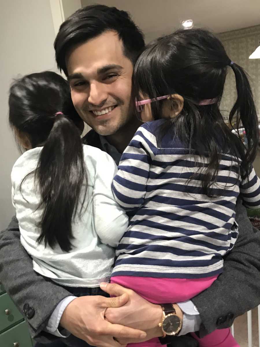 Man smiles as he holds two foster daughters in his arms