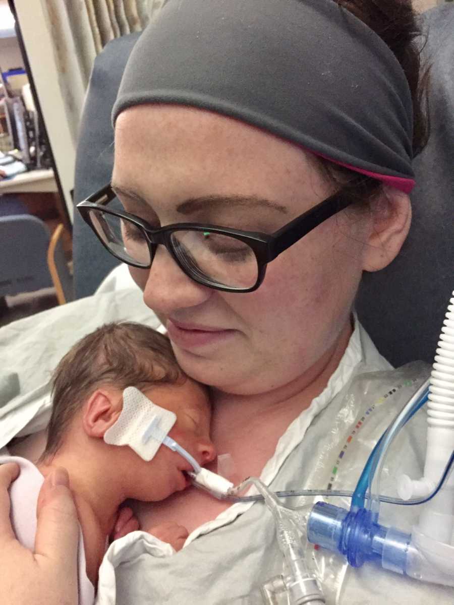 Mother smiles as she looks down at intubated newborn laying asleep on her chest